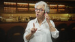 © Krakenimages.com - Elderly woman holding smartphone to her ear and giving a thumbs up gesture in a studio; warmth connection.