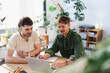 © Studio Marmellata - Two men collaborate on a project at a desk, using a laptop and notebook. They are engaged in discussion and planning, surrounded by plants in a bright, modern office space.