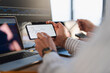 © Studio Marmellata - A person analyzes financial charts on a smartphone while another person uses a laptop, suggesting a collaborative trading or investment session.