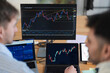 © Studio Marmellata - Two individuals analyze financial market charts on multiple screens, indicating a focus on trading and investment strategies.