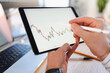 © Studio Marmellata - A person uses a stylus to interact with a financial chart displayed on a tablet, with a laptop in the background.