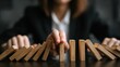 © Adip - Business professional stops a row of wooden dominoes from falling to prevent a chain reaction.