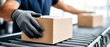 © pvl0707 - Person guides light brown cardboard box onto conveyor belt in a brightly lit workspace with grey rollers
