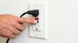© Nataly - Hand pressing reset button on electrical outlet with plugged-in power cord indicating safety features. Electrical outlet includes GFCI functionality ensuring protection against shock hazards.