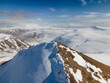 © AmazingAerialAgency - Aerial view of Moskardhshnukar mountain peak with hikers standing on the snowy summit overlooking a vast winter landscape under a blue sky Mosfellsbaer, Kjosarhreppur, Iceland.