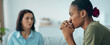 © Prostock-studio - One woman is sitting with a worried expression, while another woman speaks to her. They are in a room with light colors and some plants. It looks like a discussion about feelings.