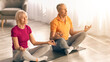 © Prostock-studio - A couple sits cross-legged on yoga mats. They are meditating in a bright room filled with natural light. The woman wears a pink shirt and the man wears an orange shirt. They focus on their breath.
