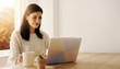 © Simone - A professional young woman in a cream knit sweater working remotely on a laptop at a light oak desk. Bright minimalist home office interior with warm golden hour light, blurred autumn foliage in the b