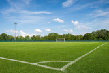 Empty soccer field with green grass and white corner line under a blue sky, professional sports pitch with goal post and stadium lights for competition and training