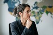 © imagezine - Professional woman in a corporate setting deep in thought against a blurred background. Suitable for editorial and international policy contexts.