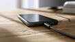 © Mikhail Vorobev - Modern smartphone with charging cable plugged in lying on wooden surface next to laptop in bright natural light setting