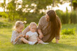 © Tina kids photo - mother with two daughters sitting on a lawn at sunset in the summer, hugging