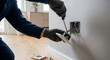 © For You Retouch - A close-up of a person wearing black gloves using a screwdriver to install a new electrical wall socket in a modern interior.