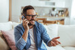 © Dragana Gordic - Happy Man Talking on Smartphone at Home Couch Smiling During Casual Phone Conversation and Remote Work