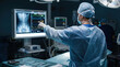 © Taras Roshchuk - A surgeon analyzes patient scans and data on a monitor while preparing for surgery. Bright lights shine down in a hospital operating room. Medical staff are nearby