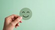© Pinit - A green happy smiley face held by hands for customer review and satisfaction survey.