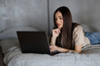 © F8  \ Suport Ukraine - A young woman works on her laptop in bed, surrounded by cozy lighting and enjoying a breakfast bowl.