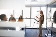 © fizkes - Middle-age businesswoman presenting information to diverse team members at conference or corporate presentation meeting in office. Business training, executive coaching, and professional development