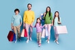 © deagreez - Happy family shopping trip with parents and three children carrying colorful shopping bags and smiling together against a bright blue studio background