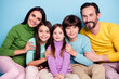 © deagreez - Smiling family portrait of parents and three children in colorful sweaters, sitting close together against a blue background showing warmth and togetherness