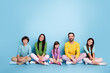 © deagreez - Family of five parents and children sitting together on floor smiling in colorful casual clothes against blue studio background
