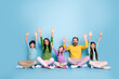 © deagreez - Happy family sitting together with raised hands against a blue background, parents and three children enjoying playful togetherness