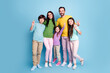 © deagreez - Happy family portrait of parents and three children smiling and making peace signs against a blue studio background