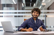 © Tetiana - Portrait of a smiling young Indian businessman signing documents at a desk in the office