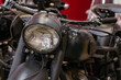 © DenisProduction.com - Detailed close-up view of vintage motorcycle front, showcasing large round glass headlight with ribbed texture and matte black housing. Handlebars and part of fuel tank are visible against a blurred
