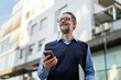 © Miljan Živković - Smiling businessman holding smart phone and laptop outdoors