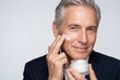 © Meow Creations - Handsome senior man applying moisturizing lotion for a male skincare routine on a white background