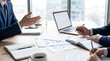 © Julie - Business people's hands at an office desk, discussing strategy, with documents, laptop and coffee, bright.
