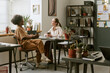 © AnnaStills - African American young adult woman and Caucasian young adult woman meeting at office desk, discussing project over coffee. Ideal for teamwork, mentoring, workplace communication