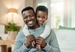 © peopleimages.com - Portrait, dad and smile with child in lounge, piggyback and bonding with son and connection in home. Happy, family and affection for kid in house, childcare or black man with boy and support on break