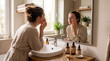 © alex - A woman in a robe applies face cream to her cheek while looking into a bathroom mirror. Skincare bottles, a sink, and a potted plant are positioned on a wooden counter in the foreground.
