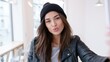 © Дмитрий Баронин - Young woman with long brown hair wearing a black beanie and leather jacket poses playfully, blowing a kiss towards the camera in a bright, modern indoor setting with soft lighting