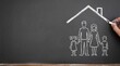 © majid - Hand drawing a symbolic chalk house over a family illustration on a blackboard, representing home protection and security.