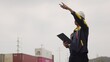 © HarryKiiM Stock - A logistics supervisor with a walkie-talkie directs crane operations, pointing upwards while coordinating cargo movement at an industrial shipping port.