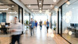 © Vhagar - A modern office corridor bustling with people. Blurred motion creates a dynamic atmosphere, with glass walls and contemporary decor highlighting a collaborative work environment.