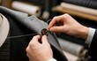 © erina - Tailor sewing a button onto a grey suit jacket in a workshop.
