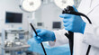 © DebbyMelindaYanti - A medical professional in blue gloves holds an endoscope ready for a medical procedure. Sterile hospital room with diagnostic equipment