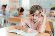 © chokniti - Back to school and education concept of schoolchild with glasses writing in notebook classroom study education learning student child writing notebook desk school