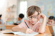 © chokniti - Back to school and education concept of young student boy glasses writing notebook classroom education school child desk schoolroom learning study pencil concentration focused thoughtful portrait