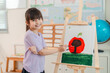 © chokniti - Back to school and education concept of smiling girl painting apple on easel in classroom art lesson