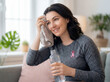 © Aurora Aesthetics - Breast cancer survivor woman wiping forehead with towel pink ribbon awareness female with dark hair smiling holding water bottle after workout at home recovery rehabilitation strength and resilience