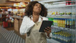 © Krakenimages.com - Young african american woman baker in restaurant wearing apron holding a tablet, hand clutching throat for choking and visible discomfort; stress illness.