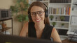 © Krakenimages.com - Woman with headphones and glasses smiling and typing at computer monitor in office; focused productivity.