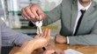 © fizkes - Closeup of realtor agent handing house keys to clients couple after successful property purchase. Home ownership, real estate transaction, property investment, apartment tenancy and renting concept