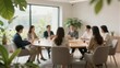 © mihrzn - A group of professionals discusses at a conference table in a bright, modern office with lush green plants and natural light.