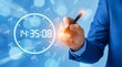 © Nurjahan - A businessman in a blue suit using a digital pen to interact with a large digital clock and various icons on a blue background with bokeh lights